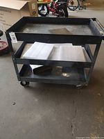 Front view of metal utility cart showing three shelves and casters