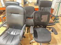 Group of five black swivel office chairs: faux leather, mesh back, fabric, all on casters