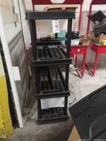 Full view of 4-tier black plastic shelving unit with printer at bottom and electronics on upper shelves