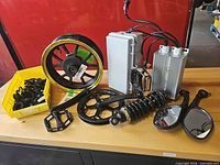 All parts laid out on bench: wheel, controllers, shock, crankset, pedals, mirrors, bin of spacers
