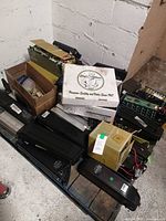 Pallet with multiple black plastic e-bike battery housings, cardboard boxes containing open cell modules and wiring