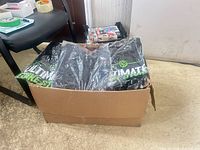 Cardboard box containing multiple sealed black graphic T-shirts with green Ultimate Bike Store logo visible