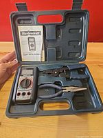 Open case showing multimeter, crimper-stripper, pliers and manual fitted in molded compartments