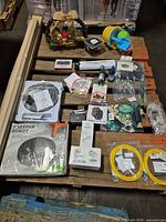 Overview of lot showing robot vacuum box, patch cords, placemat, boxed shakers, fairy lights, ink, brake pads and other accessories on pallet