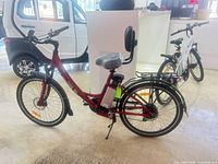 Side profile of red Daymak Paris Long Range electric bicycle showing step-through frame, battery, rear rack with backrest, 26 in wheels, front disc brake, fenders