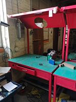 Full view of red metal workbench with teal surface, overhead hood, drawer and accessories