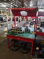 Full view of workbench showing red frame, green top, drawer, overhead hood, caster feet