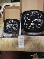 Two Trintec altimeter-style wall clocks in boxes on workbench