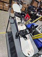 Full view of snowboard with bindings attached, showing deck graphics and general wear