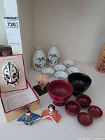 Group shot of all items: sake bottles, cups, lacquer bowls, masks, dolls