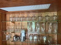 Overview of glassware on shelves: snifters, tumblers, shot glasses, pewter jugs