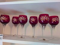 Front view of six Bohemian red floral goblets aligned on shelf