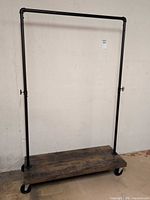Full view of clothing rack showing pipe frame and wooden wheeled base