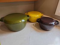 Three lidded enameled cast iron pots in green, yellow, brown