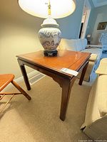 Full view of square wooden end table with lamp on top