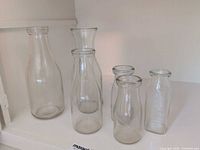 Six clear glass vessels on shelf