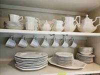 Shelved set showing stacks of plates, platter, cups, nappies, cream and sugar, teapot, pitcher