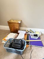 Overall view of lot on carpet showing waste basket, telephone in blue basket, piles of paper products