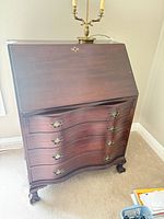 Front view of dark wood secretary desk with closed drop-front and four serpentine drawers