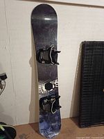 Full view of snowboard standing vertically showing deck, bindings, and overall wear