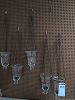 Five glass tealight holders hanging on pegboard wall, showing clear glass cups and attached metal chains