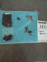 Overview of two bags and loose gemstones on blue cloth next to lot tag