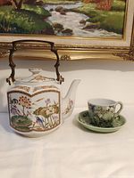 Teapot, cup and saucer grouped beneath framed painting