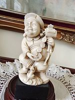 Front view of ivory-tone Chinese prosperity figurine holding coins and ingot on dark wood stand