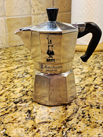 Full view of closed espresso maker showing brand logo, handle, overall wear