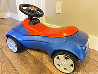 Side view of blue and red BMW ride-on push car showing wheels and body