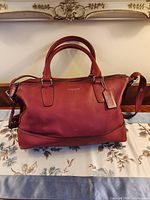 Front view of red Coach leather satchel showing handles, zipper, hangtag