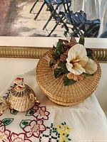 large lidded basket with floral accent beside small bird trinket box on embroidered cloth