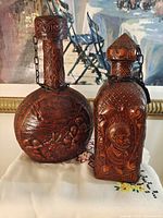 Front view of both leather-covered glass decanters showing main embossed designs and stoppers