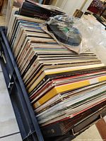 Side view of crate showing large quantity of upright LPs, protective plastic and a few loose records on top