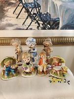 Front view of all seven Japan-marked porcelain child figurines displayed on cloth