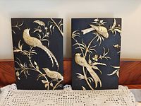 Pair of black wood plaques with gold relief birds and foliage displayed side by side