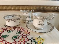 Teacup on saucer, creamer, sugar bowl showing pattern and script