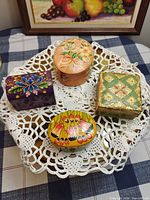Group shot of all four hand-painted trinket boxes on doily