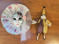 Mask and jester doll side by side on wood surface