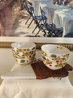 Stacked Pfaltzgraff bowls beside wood-marble tray in front of wall art