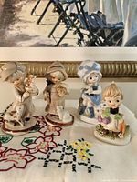Group shot of all four porcelain child figurines on embroidered cloth