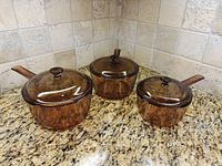 Three amber glass saucepans with lids on countertop