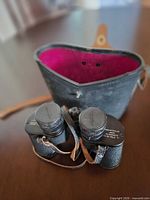 Binoculars with case interior visible, showing pink lining, neck strap, lens caps attached