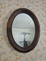 Front view of oval mirror on floral wallpaper wall
