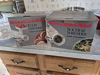 Both original KitchenAid boxes for food grinder and slicer/shredder attachments visible on countertop