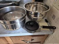 Overview of nested mixing bowls, colander, saucepan lid and handle visible