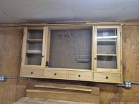 Front view of entire wall-mounted cabinet showing glass doors, pegboard and drawers