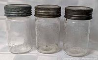 Front view of three embossed Crown glass jars with metal lids