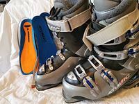 Side view of both ski boots with buckles fastened and pair of orange-blue insoles