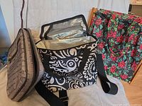All three bags displayed: gray script toiletry case, black-white insulated lunch bag, red poinsettia tote